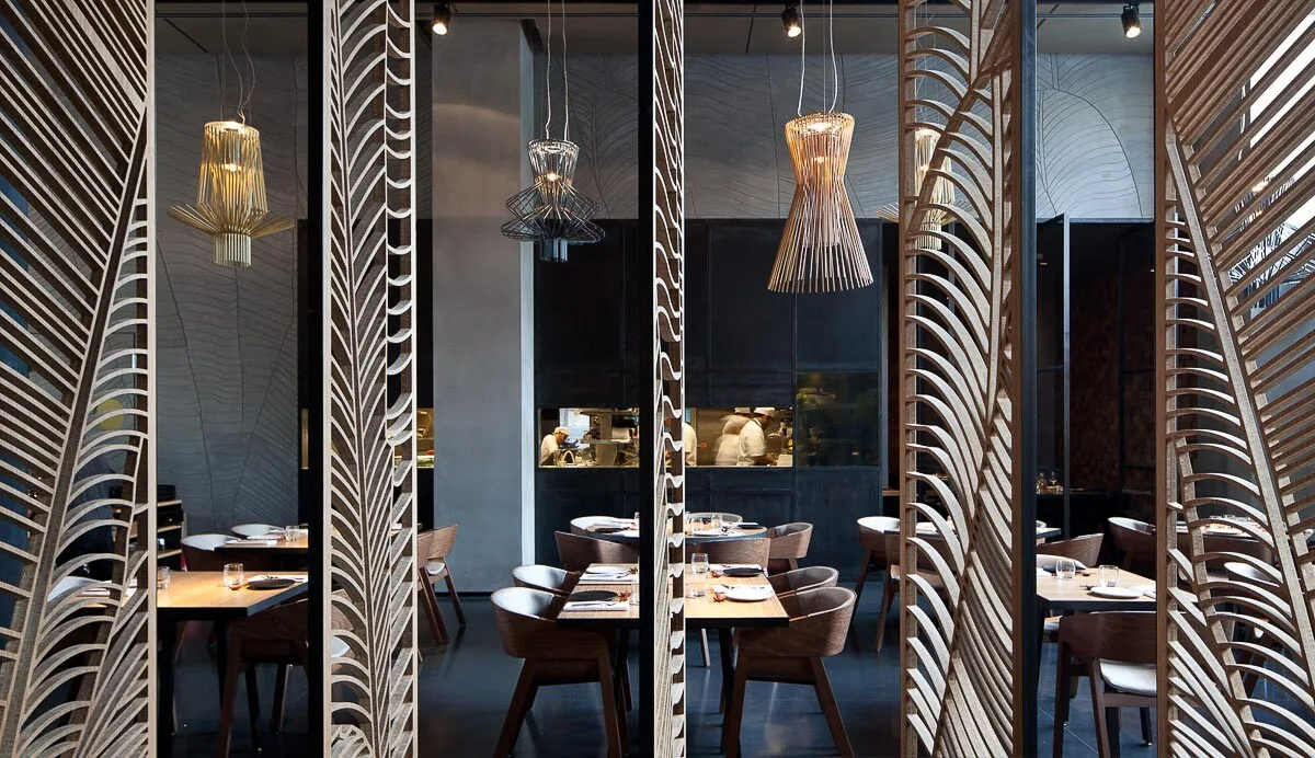 Donker restaurant met bewerkte houten scheidingswanden en sculpturale hanglampen
